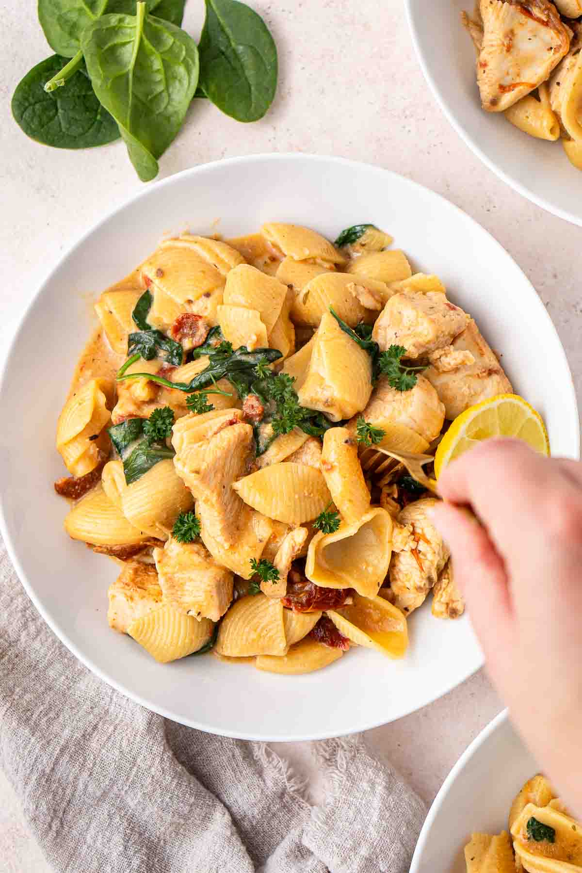 A fork taking a bite of marry me chicken pasta served in a white bowl.