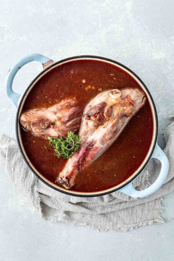 Adding the browned lamb shanks into the liquid in the pot.