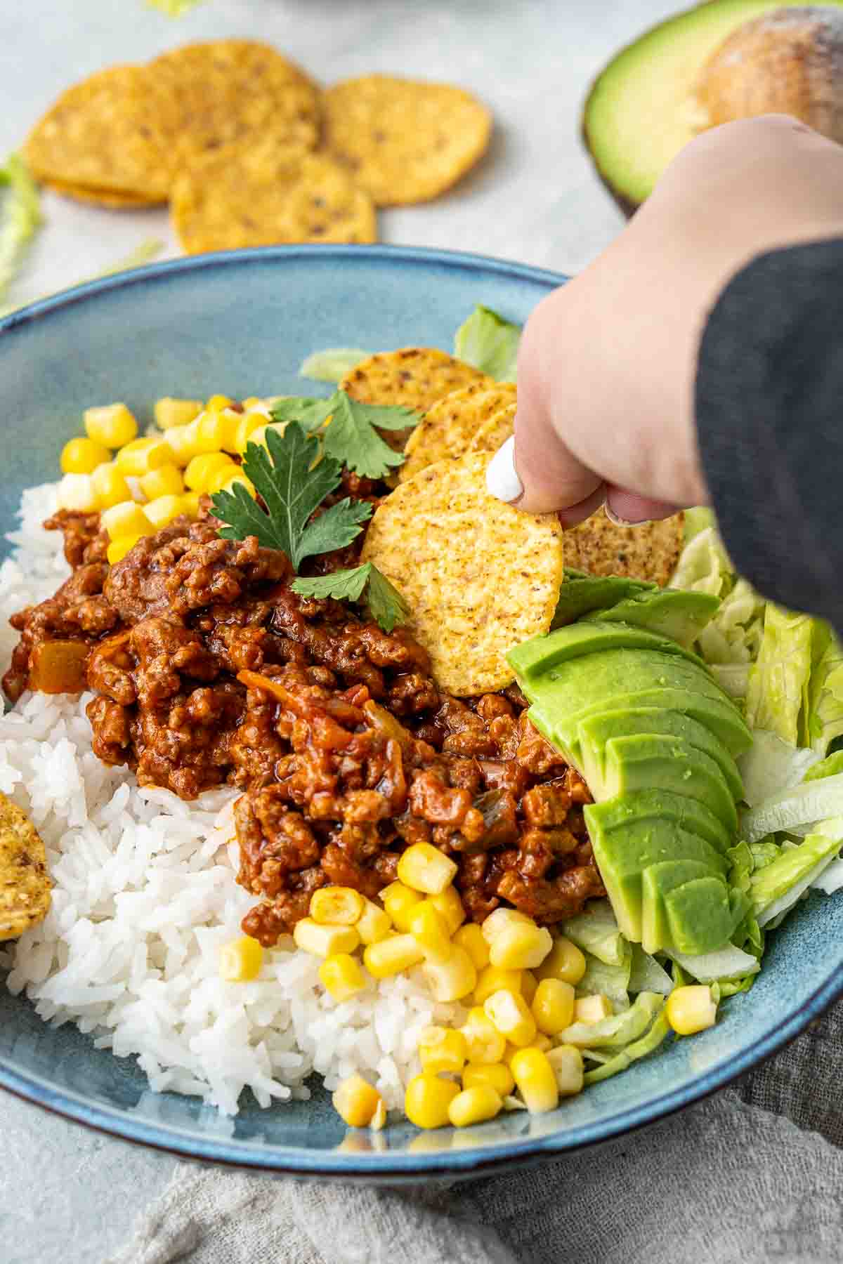 A hand taking a scoop of beef mince with a corn chip from a bowl.