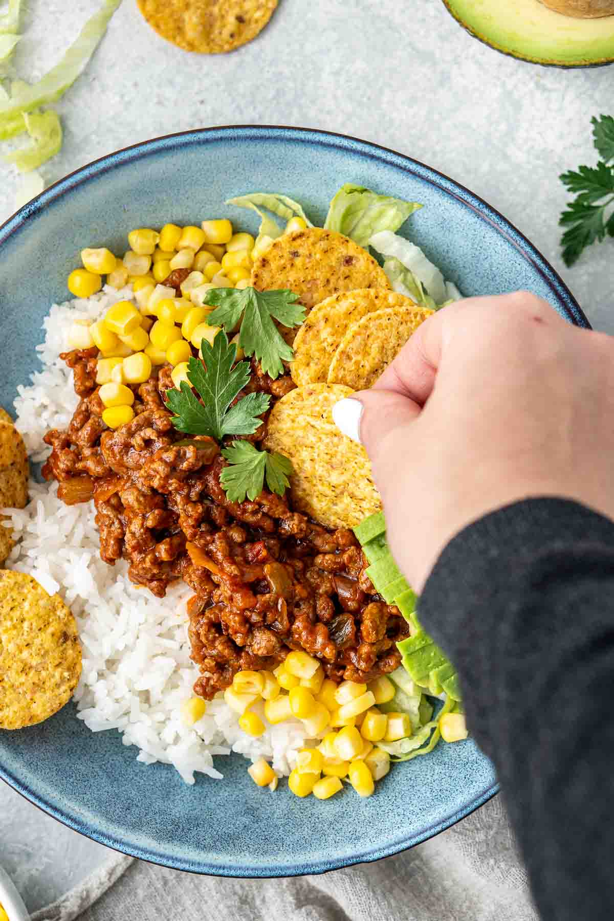 Hand taking a corn chip from a taco bowl.