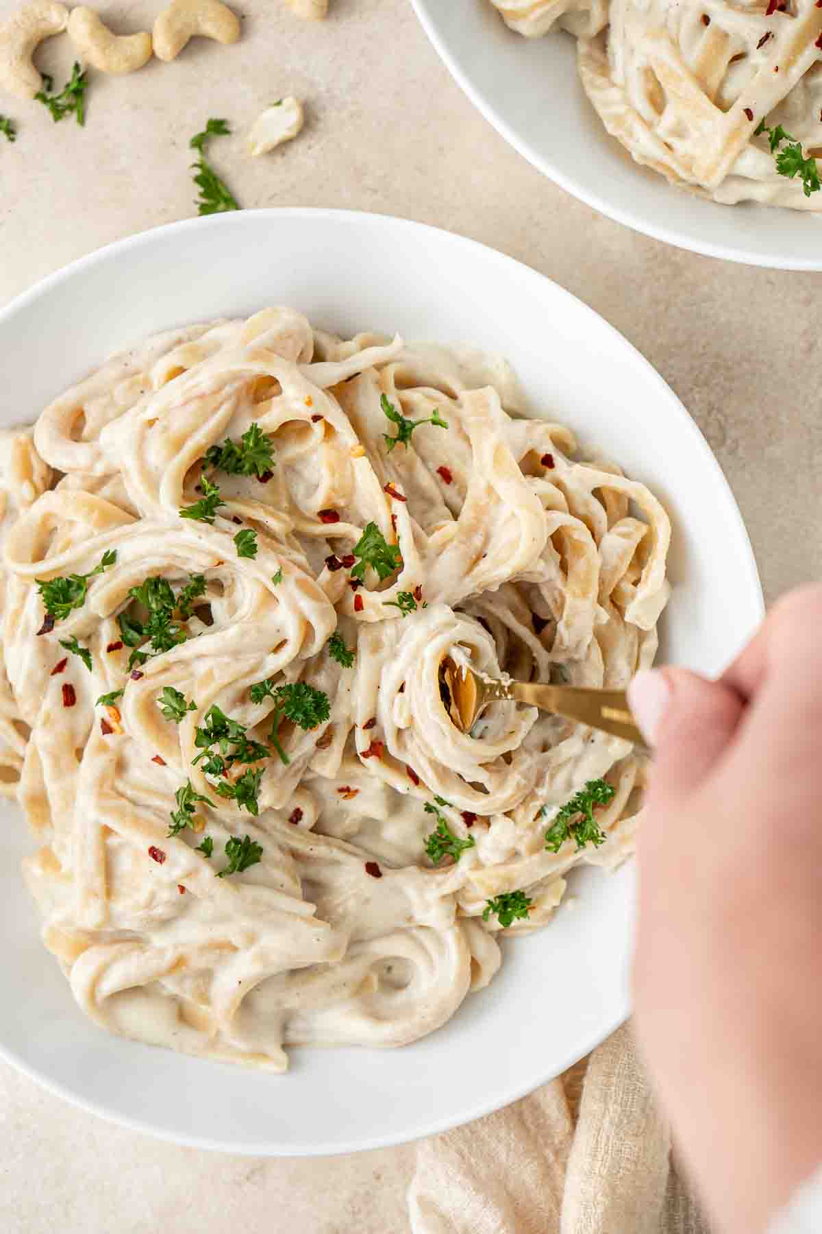 A fork taking a bite of vegan alfredo pasta from a bowl.