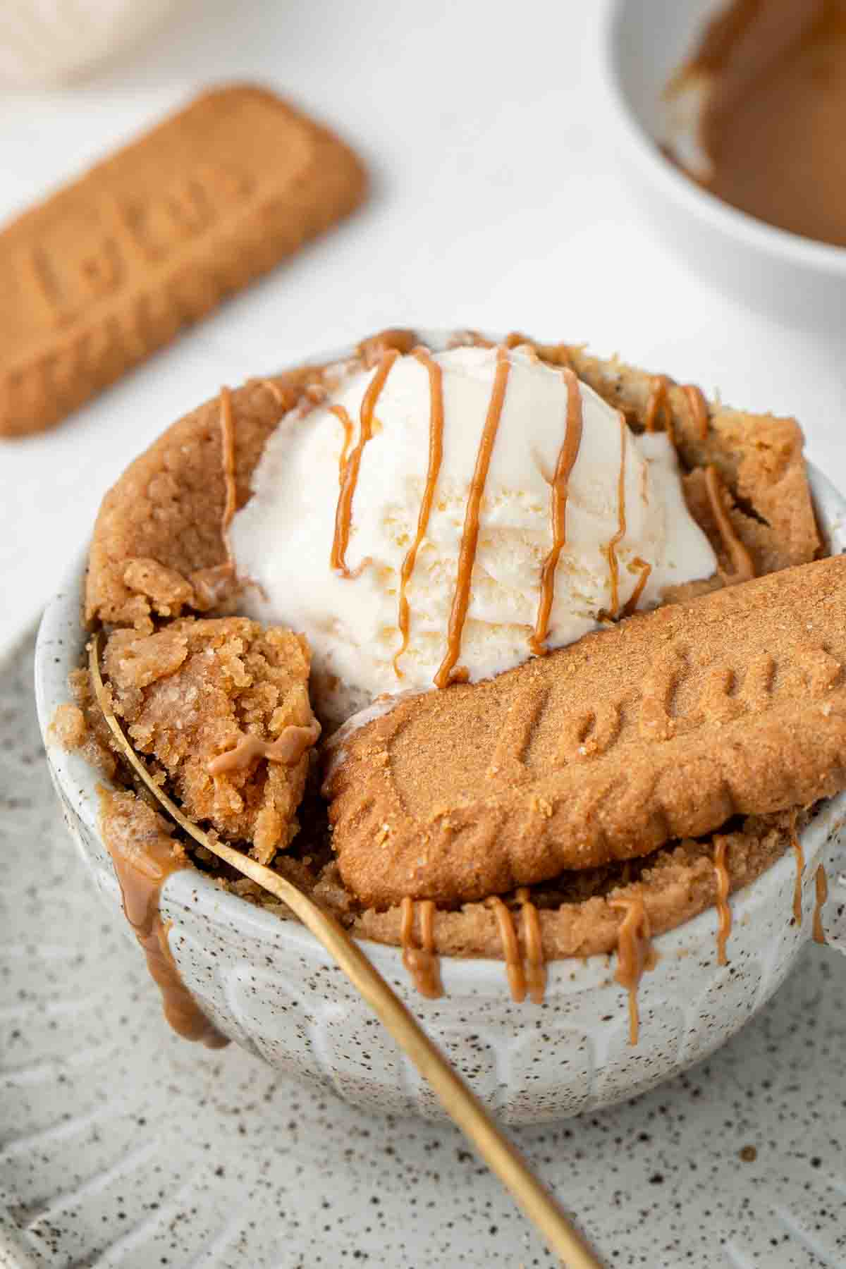 Close up of the biscoff mug cake with ice cream and a spoon taking a bite.