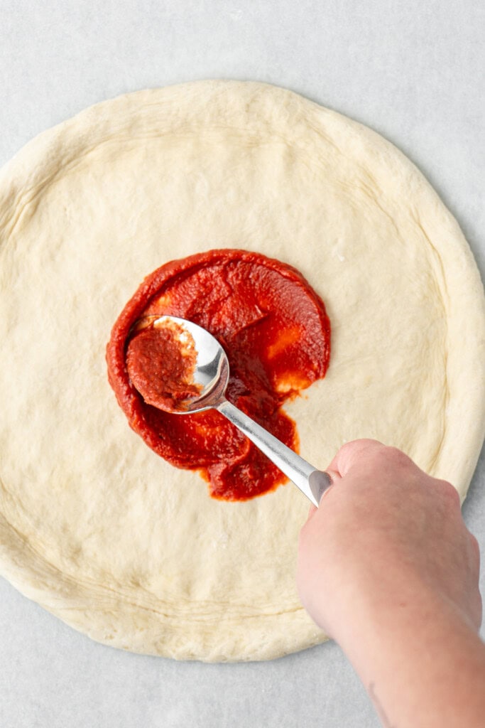 Spooning sauce onto the stretched pizza base.