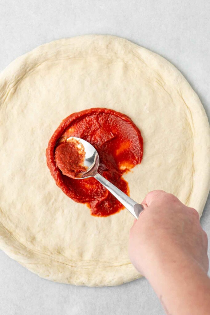 Spreading the tomato paste over the stretched dough.