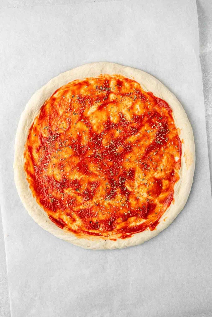 The pizza base with tomato paste and herbs.