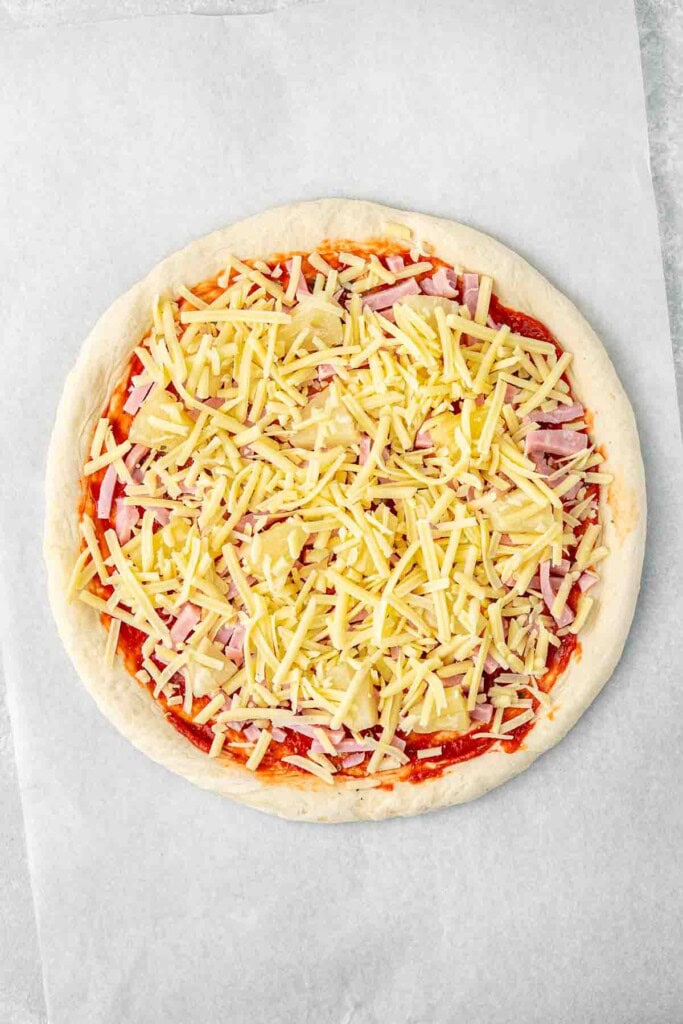 The pizza topped with cheese, ready for the oven.