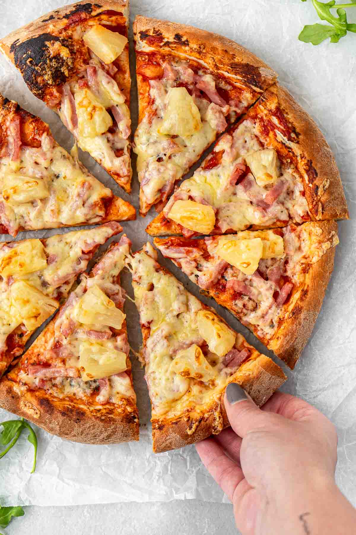 A hand taking a slice of ham and pineapple pizza.