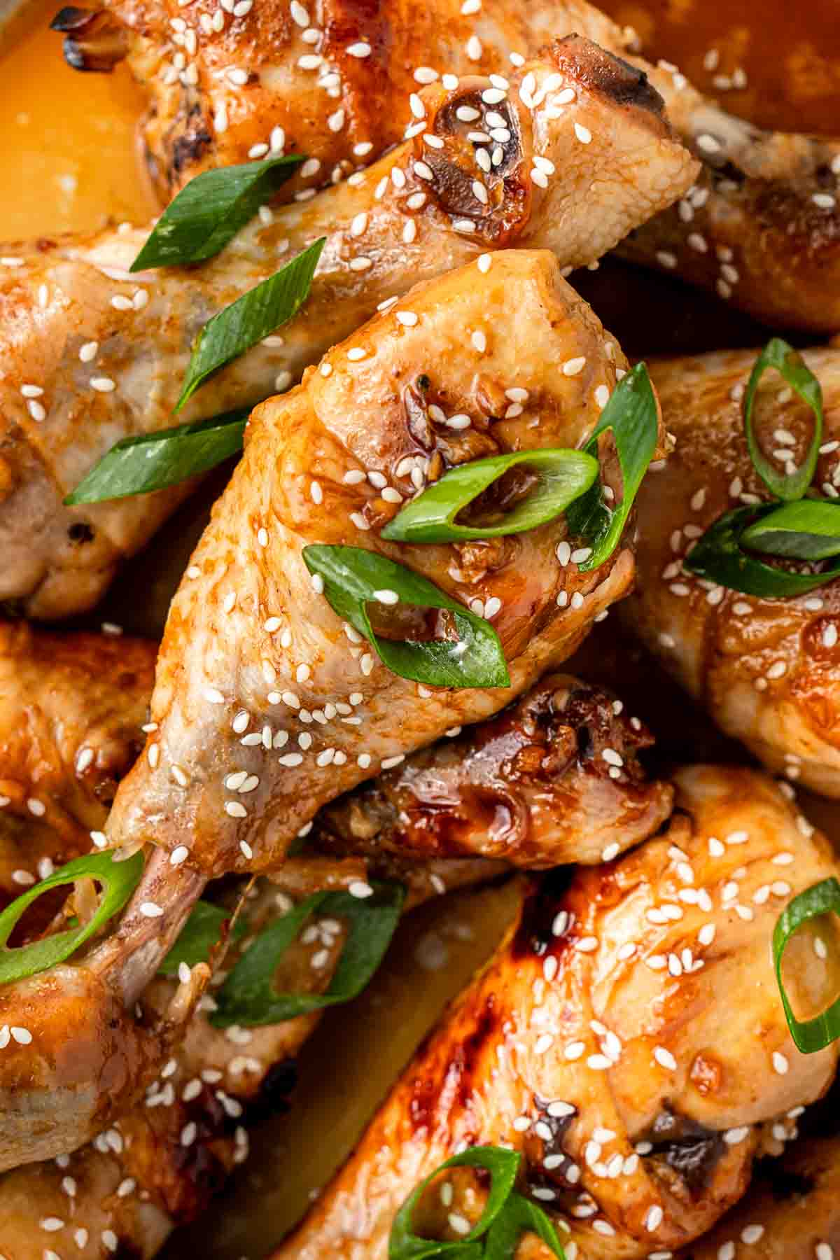 Close up of honey soy chicken drumsticks with spring onions and sesame seeds.