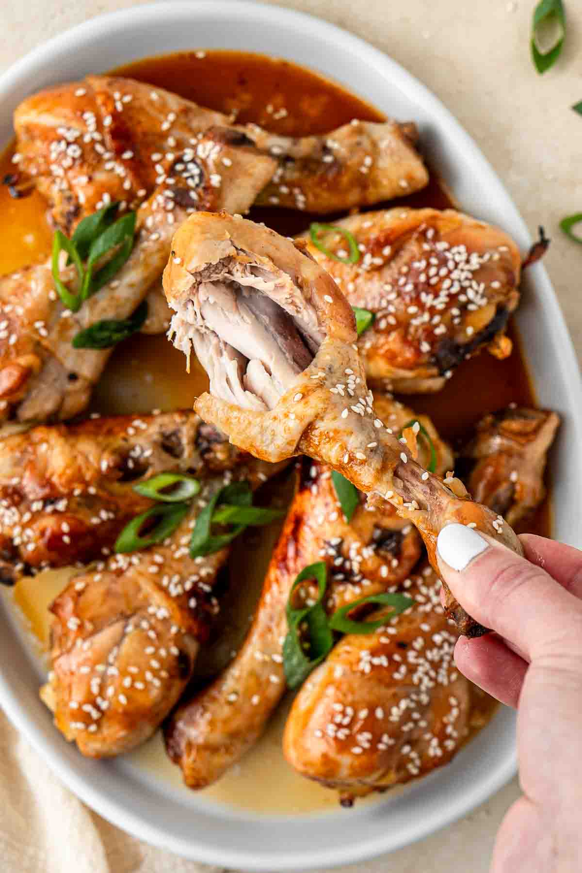 Close up of a hand holding a chicken drumstick with a bite taken.