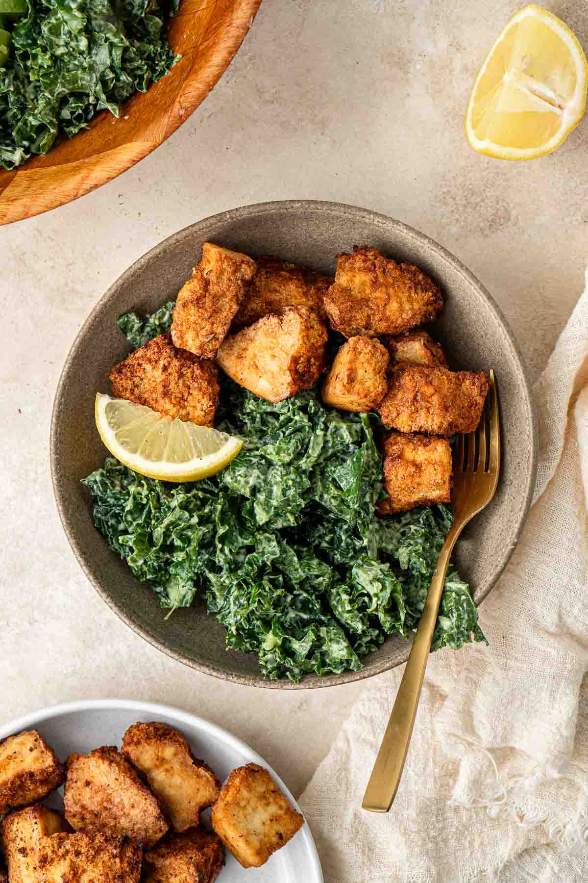 Crispy air fried tofu nuggets in a bowl with kale salad and a lemon wedge.