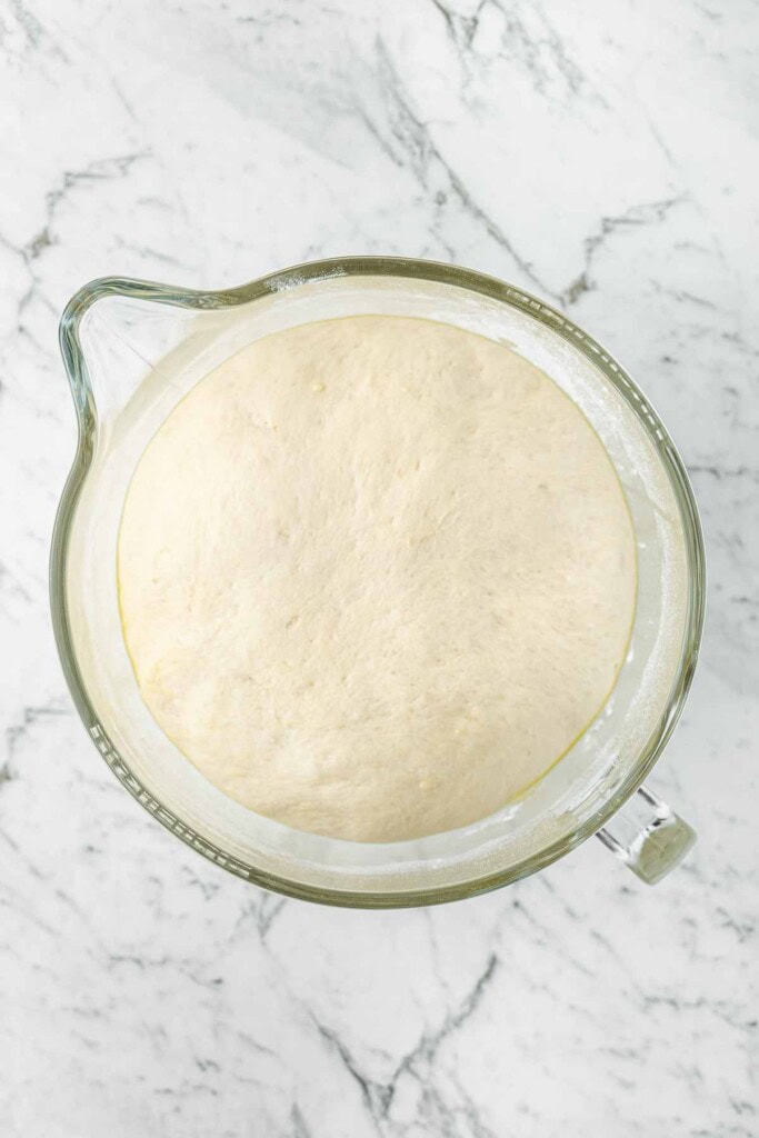 The risen pizza dough in a glass bowl.