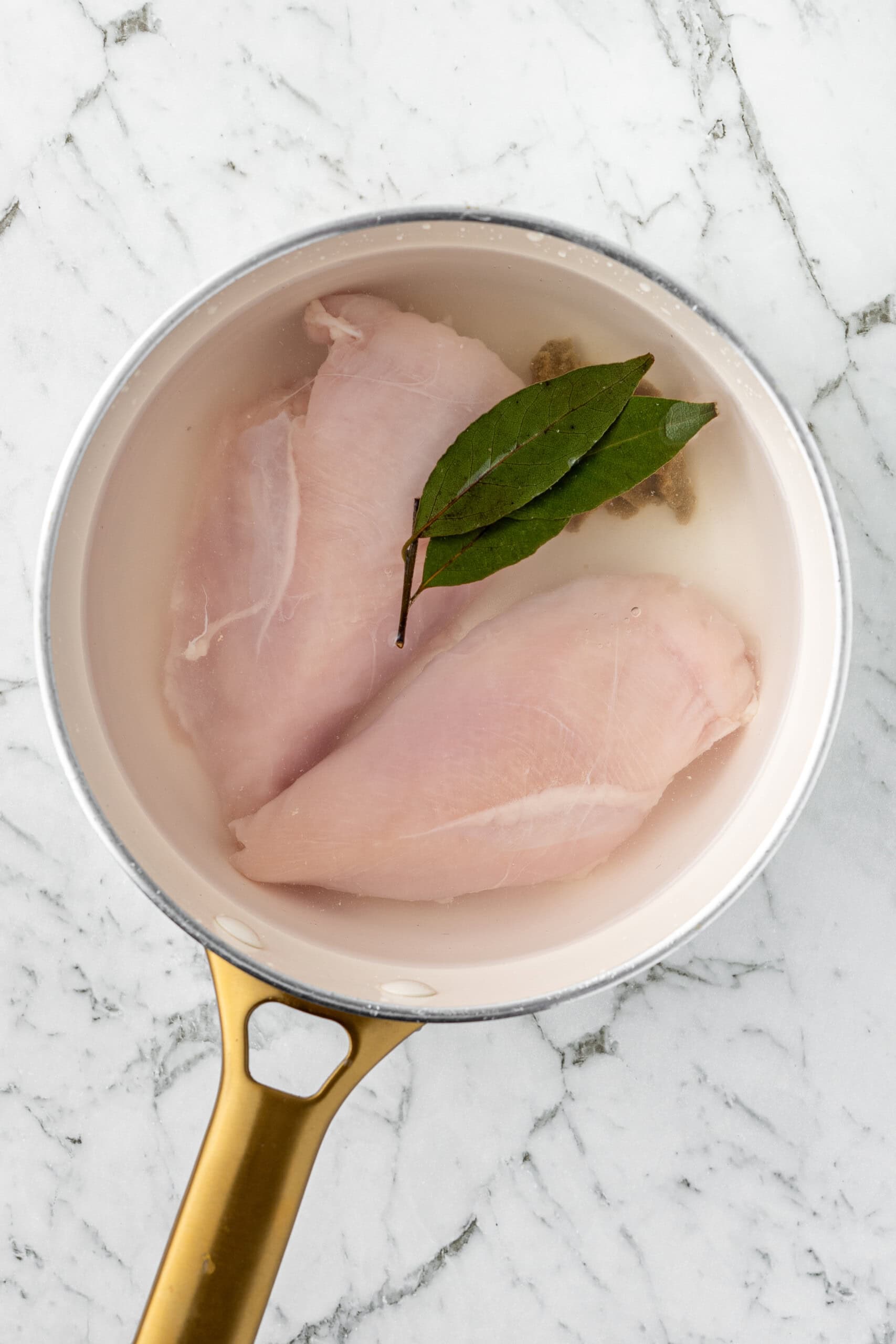 The chicken breast in the pot, covered in water with the bay leaves.