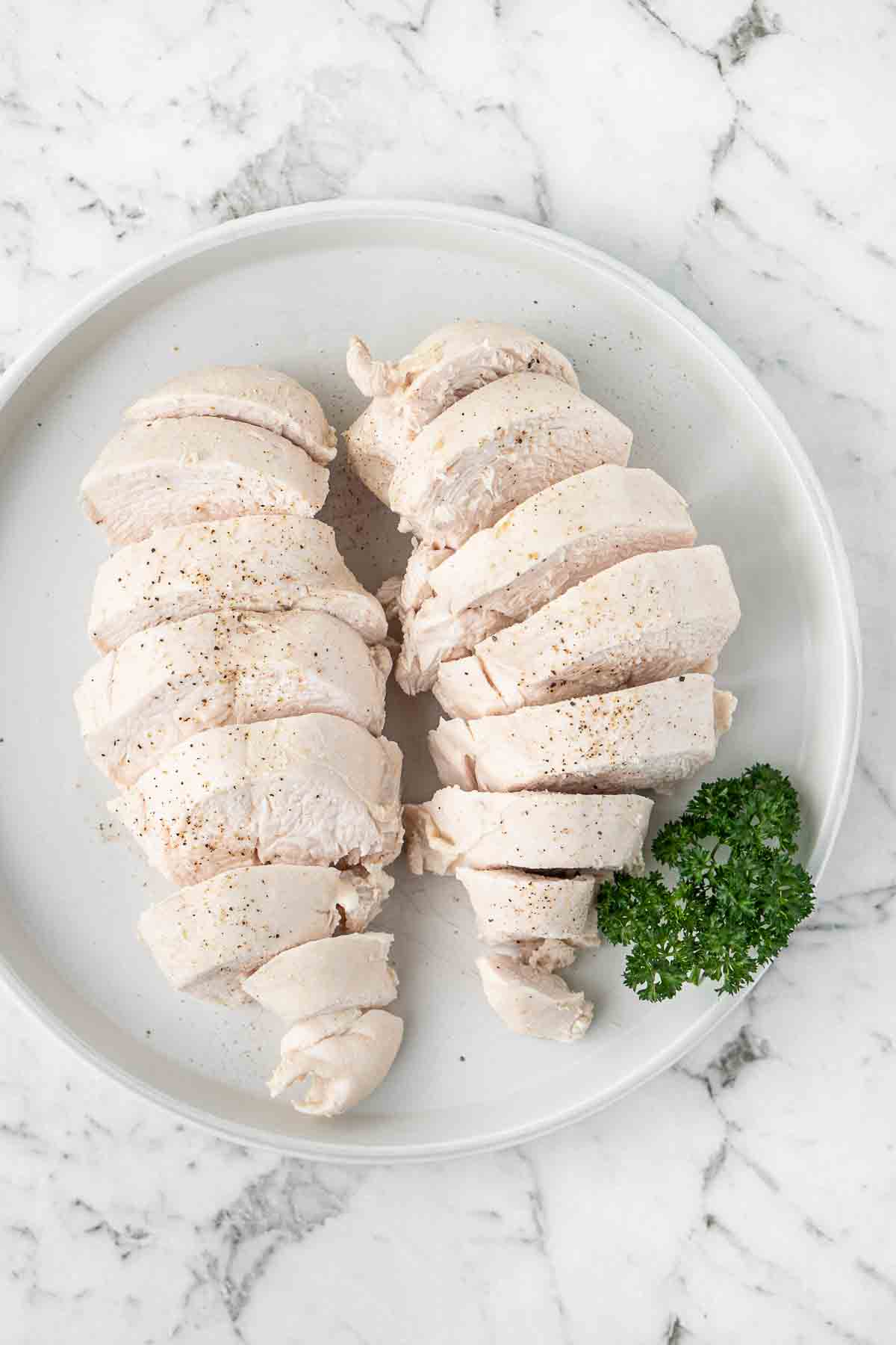 Poached chicken breast sliced on a white plate with parsley.