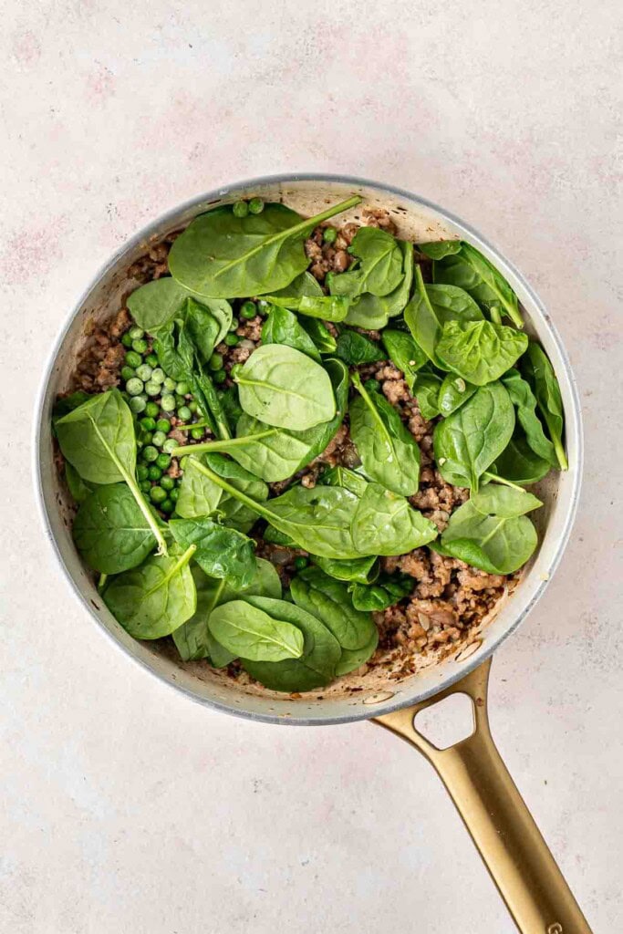 Adding the spinach and peas to the sausage in the pan.