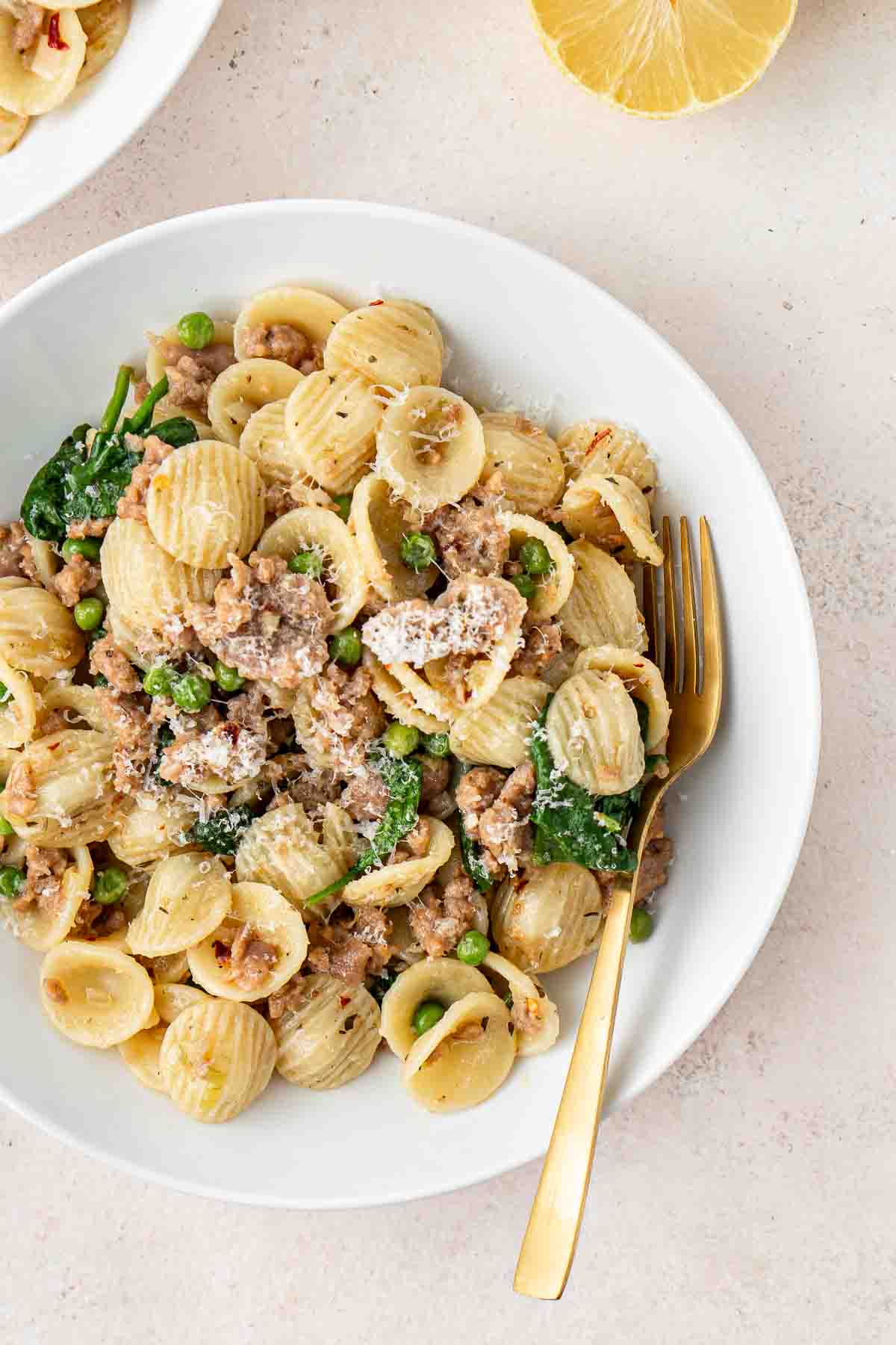 Close up of sausage and spinach orecchiette in a white bowl with a gold fork.