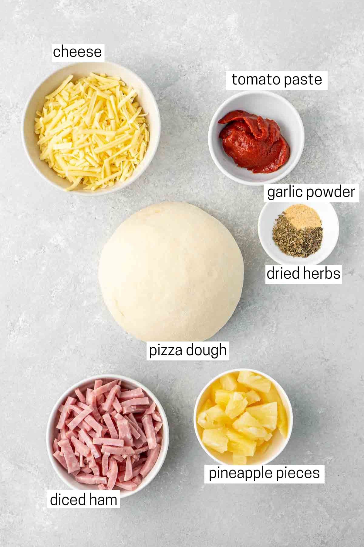 All ingredients needed to make ham and pineapple pizza laid out in bowls.