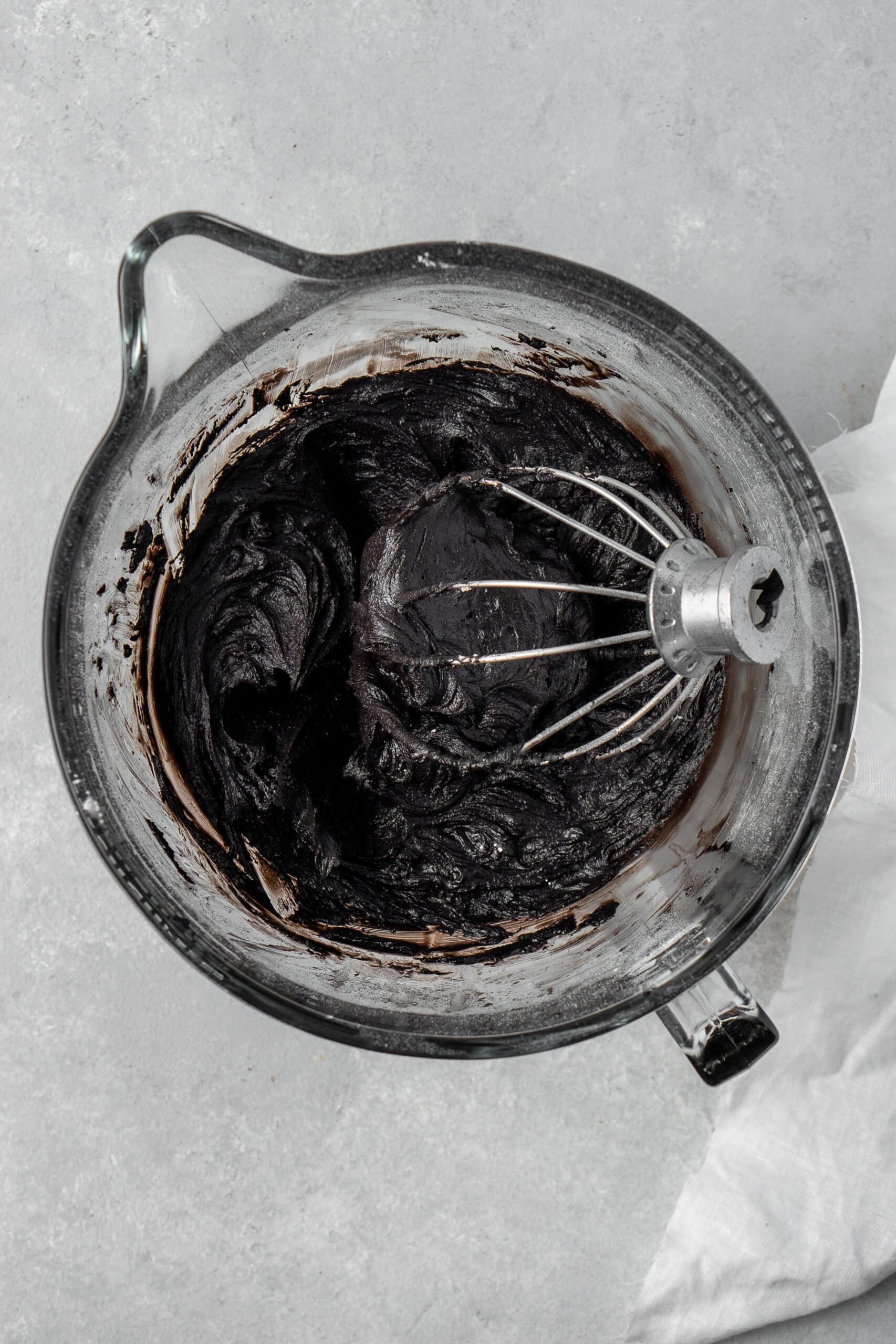 Black buttercream in a stand mixer bowl with a whisk.