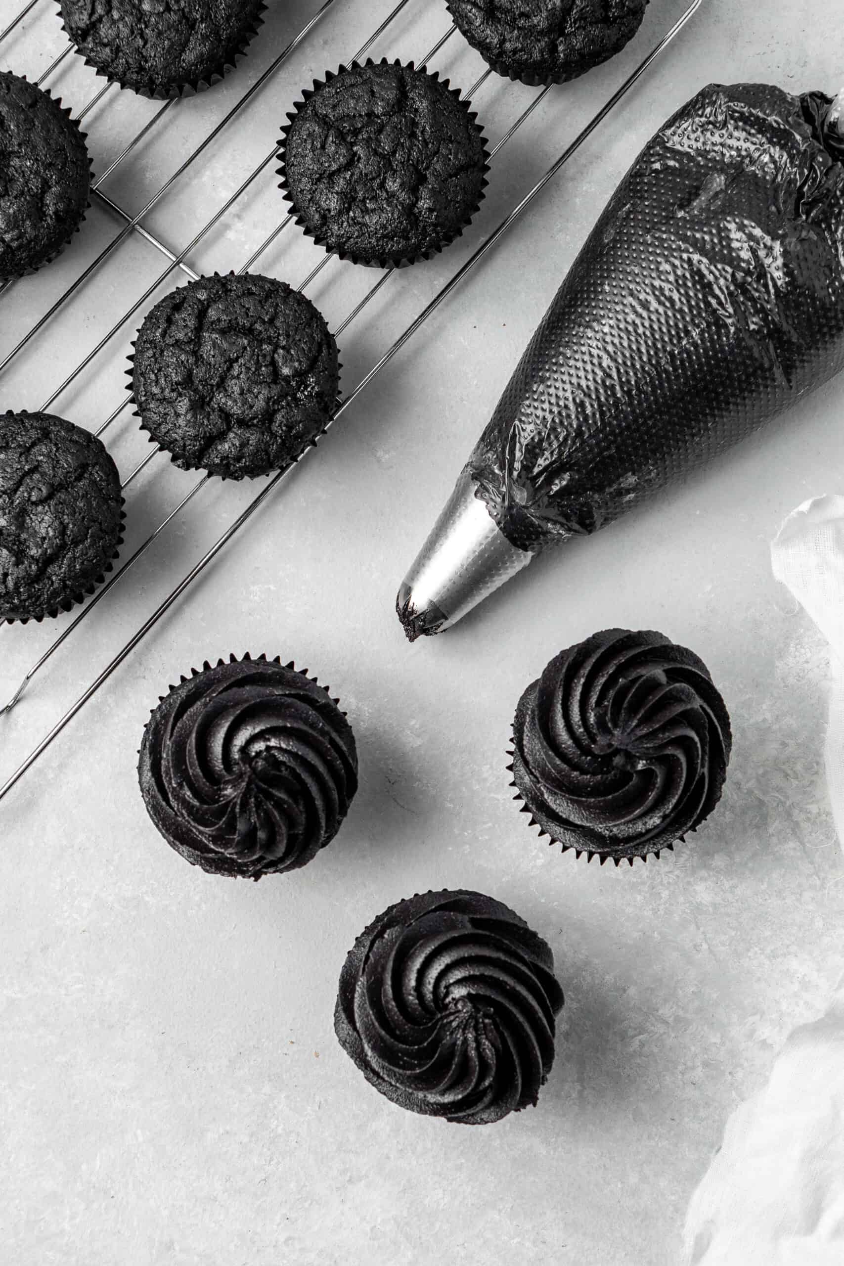 Piping swirls of black buttercream onto black cupcakes.