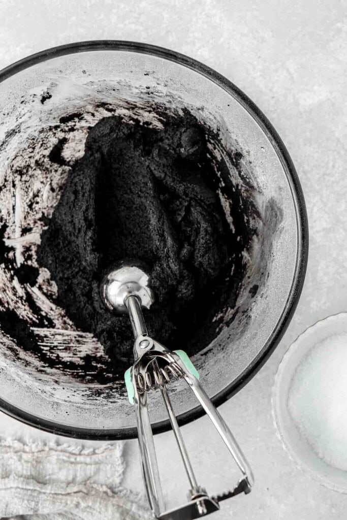 Scooping out balls of cookie dough from a glass bowl.