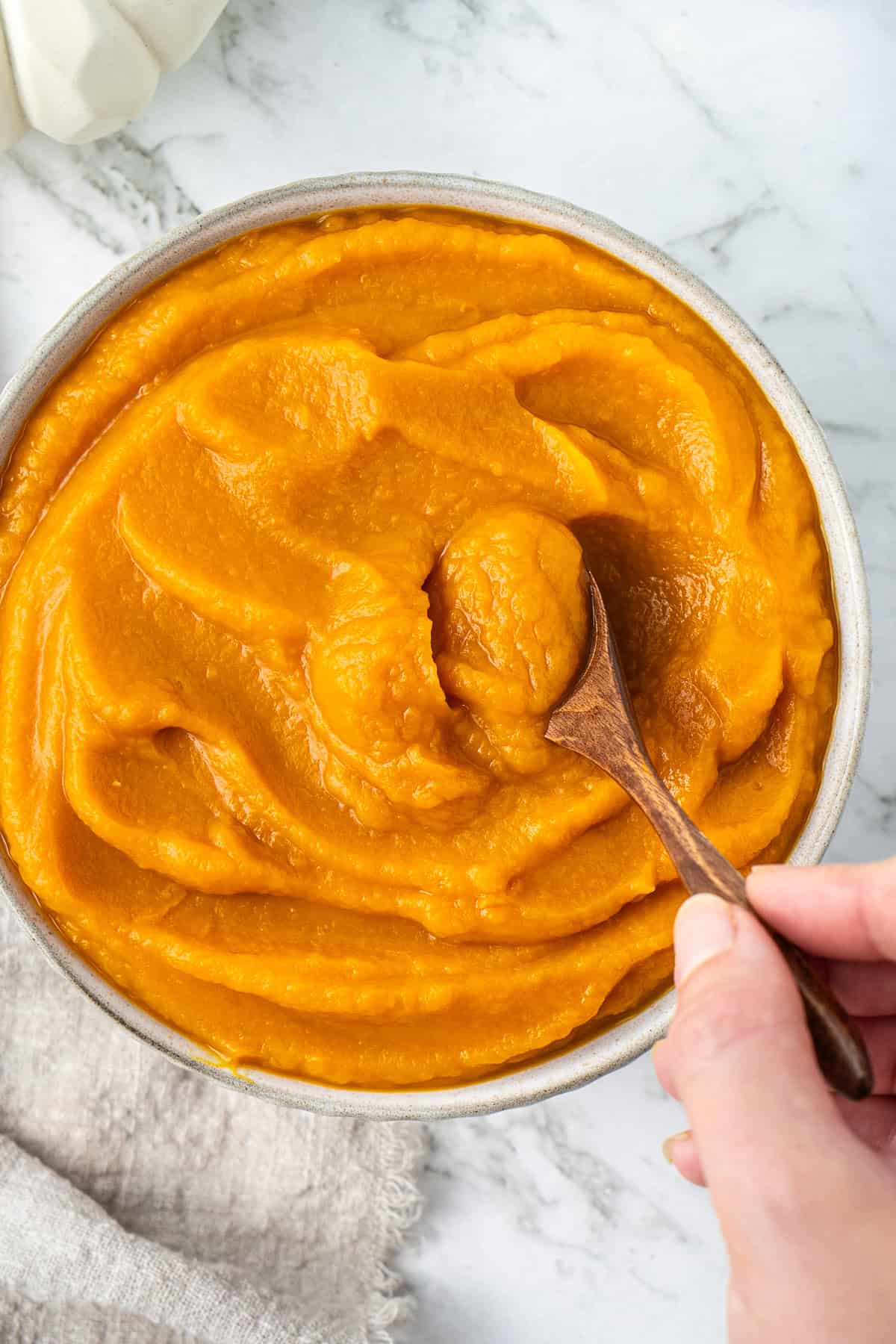 Close up of pumpkin puree in a bowl with a hand scooping some with a spoon.