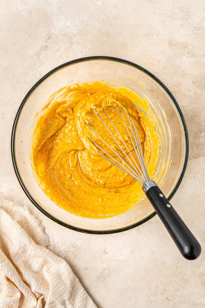 Whisking together the pumpkin doughnut batter in a glass bowl.