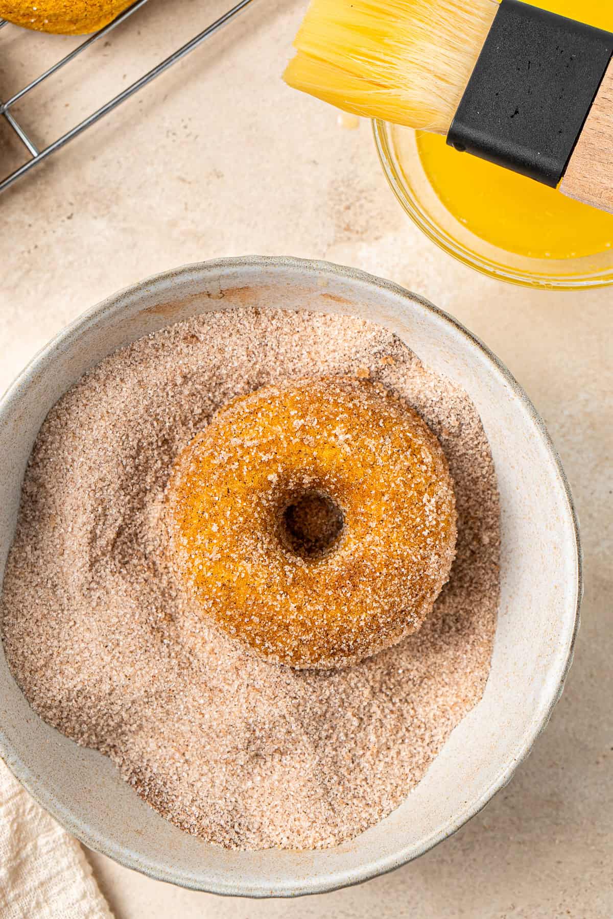 A vegan pumpkin doughnut in a bowl of cinnamon sugar being coated.