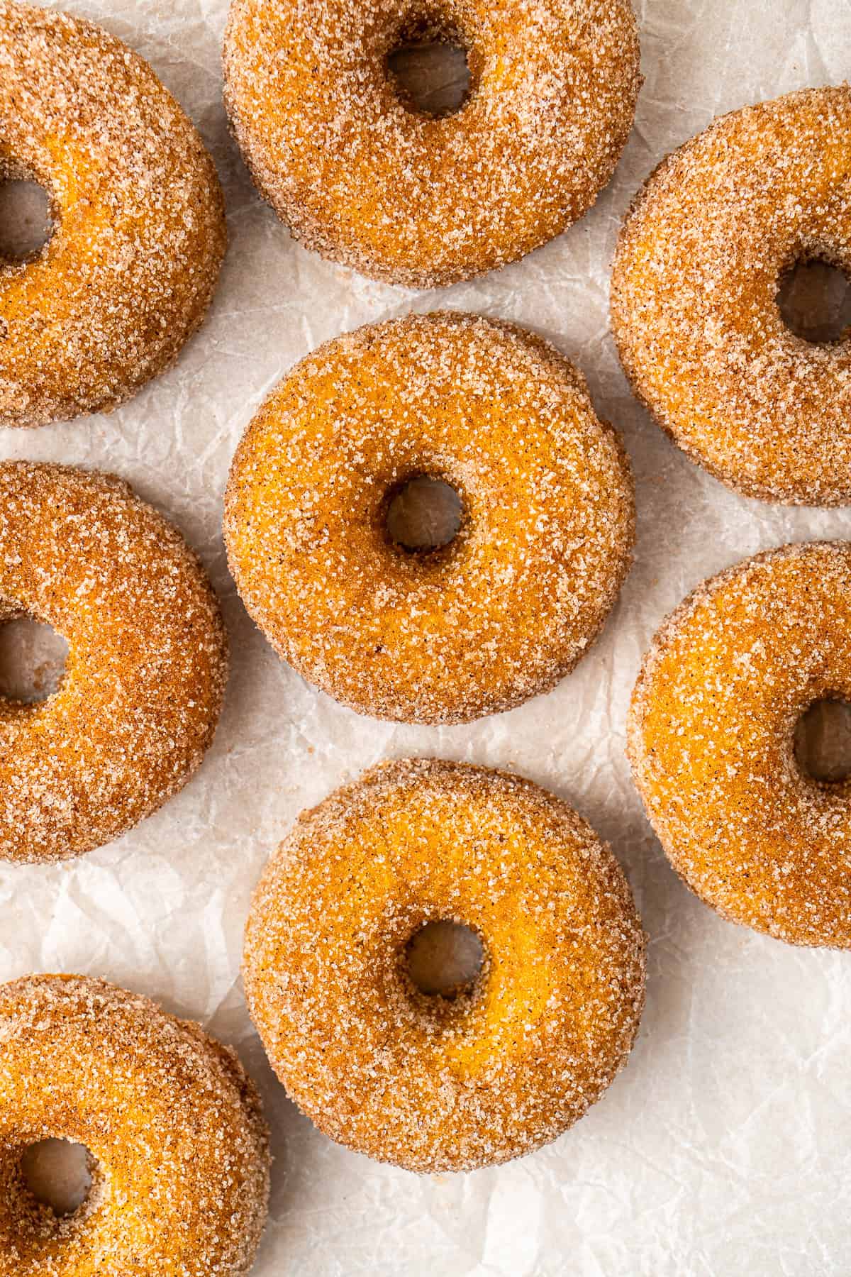 Lots of vegan pumpkin doughnuts laid out on baking paper.