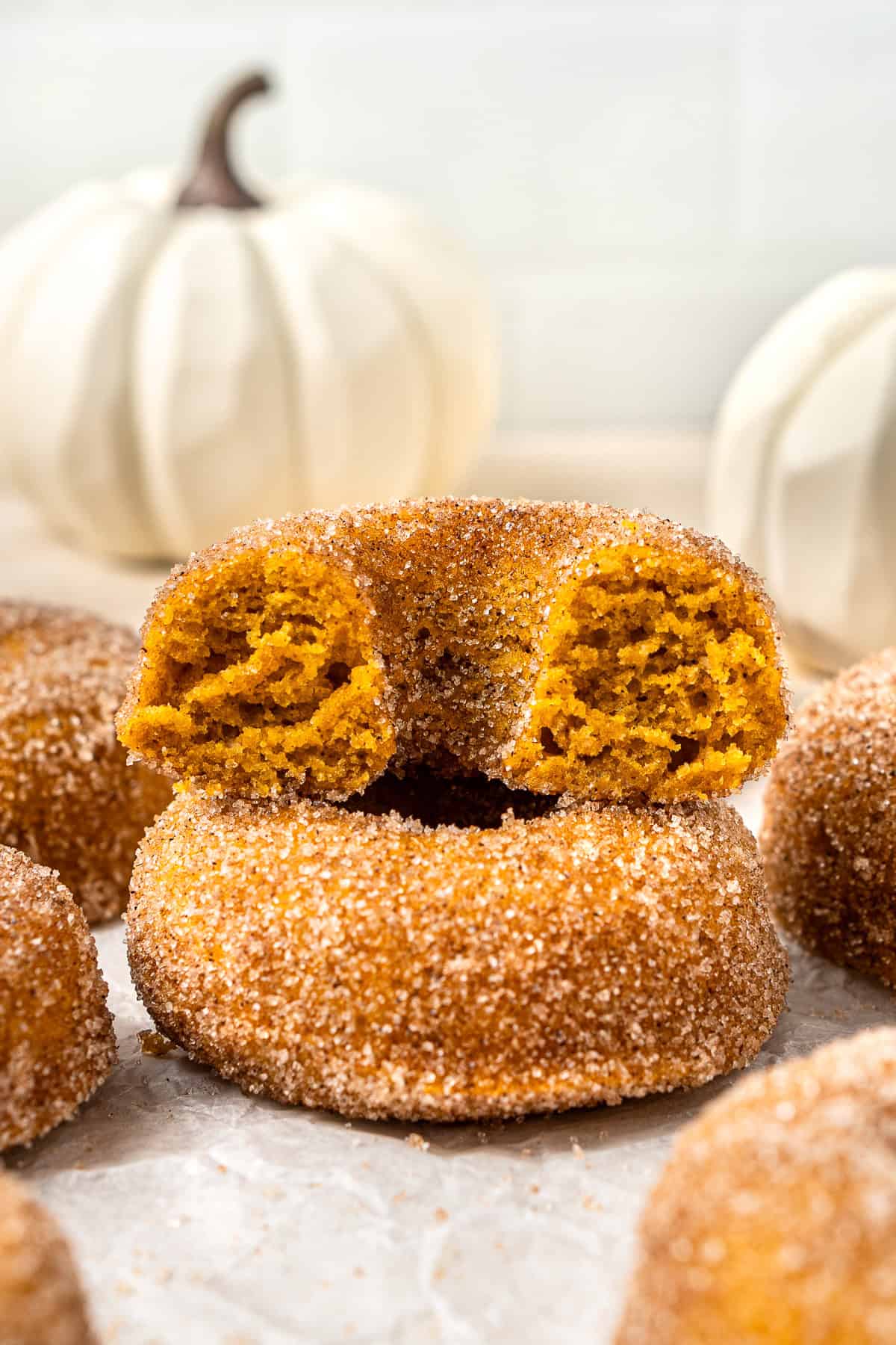 Two cinnamon coated pumpkin doughnuts, one cut in half to show the cakey texture.