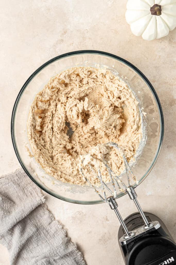 Beating together the sugars and butter in a bowl with electric mixers.