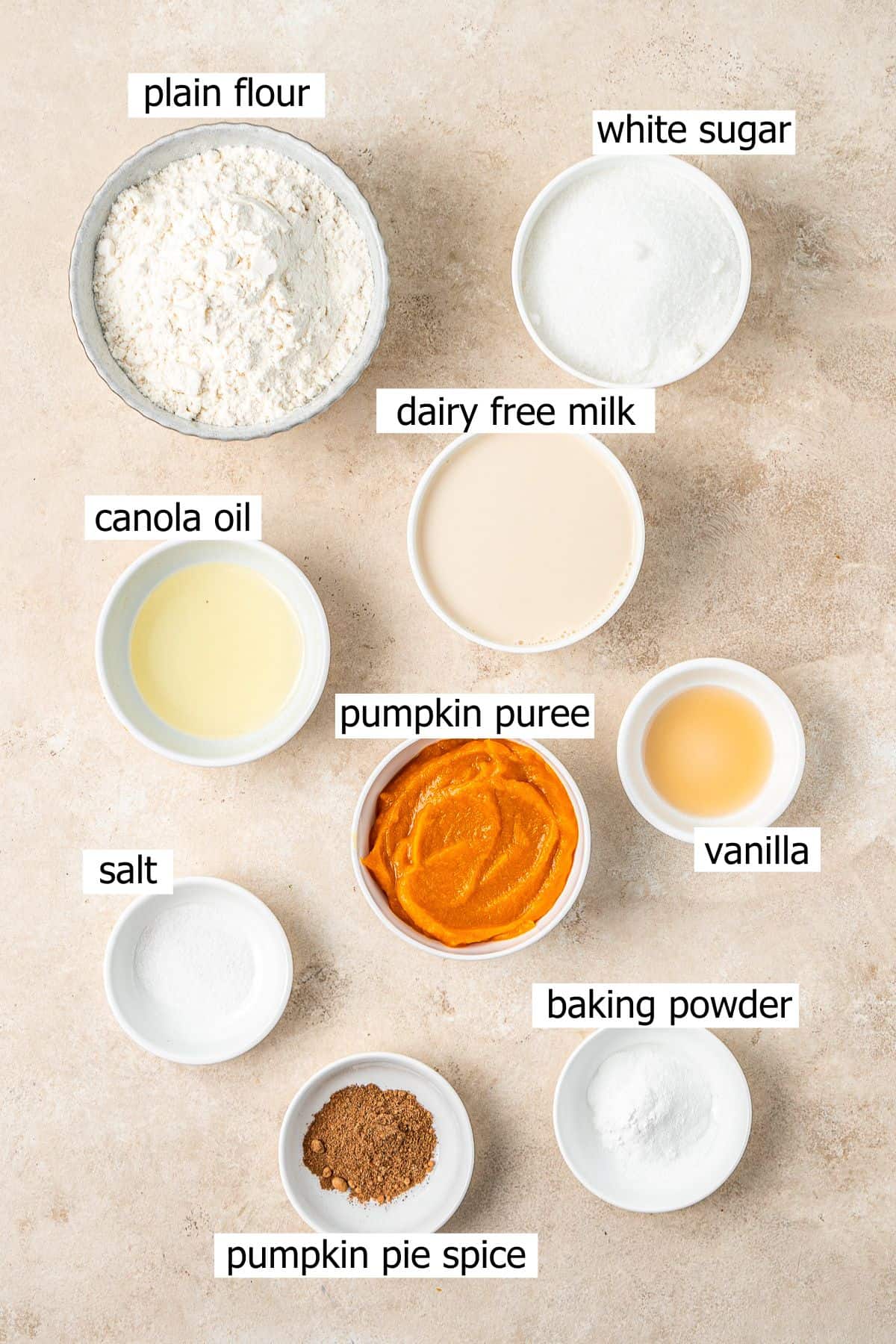 All ingredients needed to make vegan baked pumpkin doughnuts laid out in small bowls.