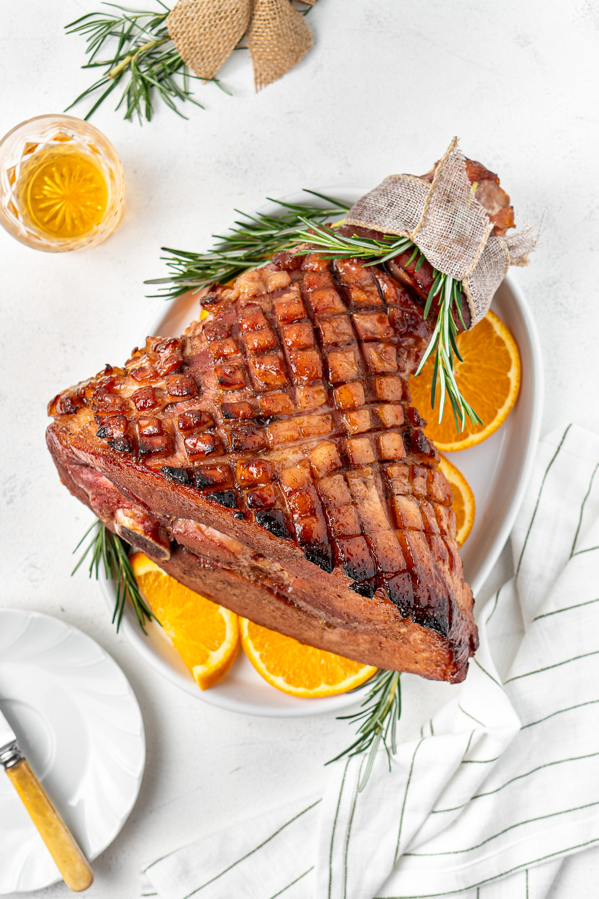 Bourbon brown sugar glazed ham on a plate with orange slices and rosemary. 