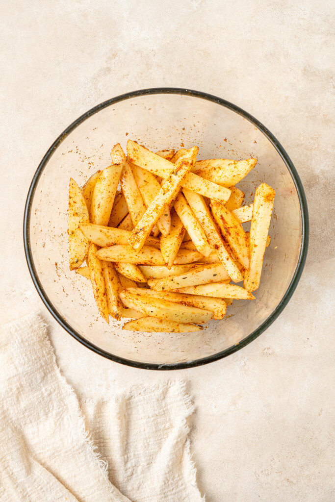 Potatoes cut into chips and seasoned in a mixing bowl.