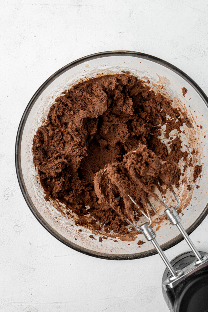 The chocolate cookie dough mixed together in a glass bowl with an electric mixer.