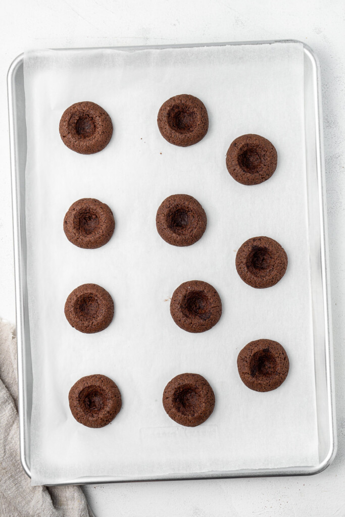 Baked chocolate thumbprint cookies on a baking tray.