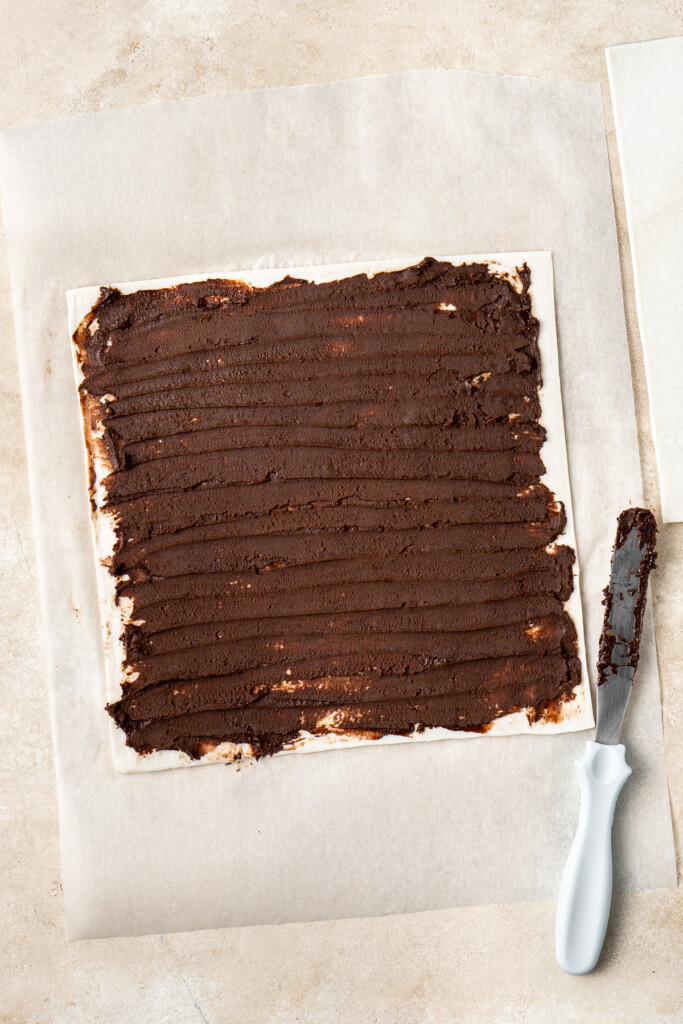 Spreading chocolate hazelnut spread over one sheet of puff pastry.