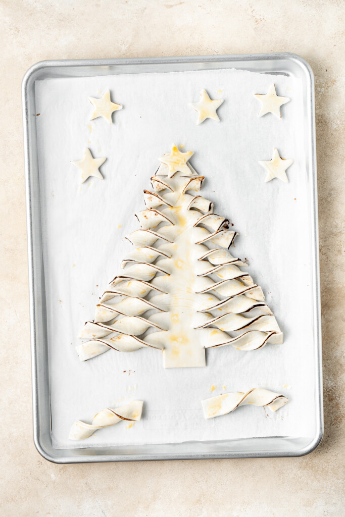 The puff pastry Christmas tree brushed with egg and on a baking tray.