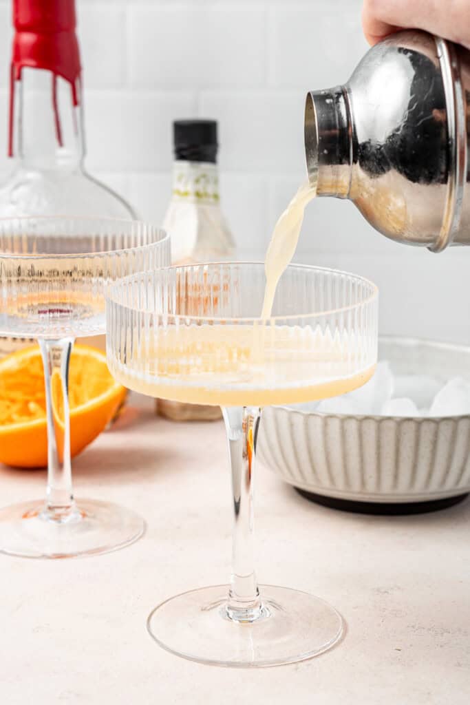 Pouring the cocktail into a coup glass.