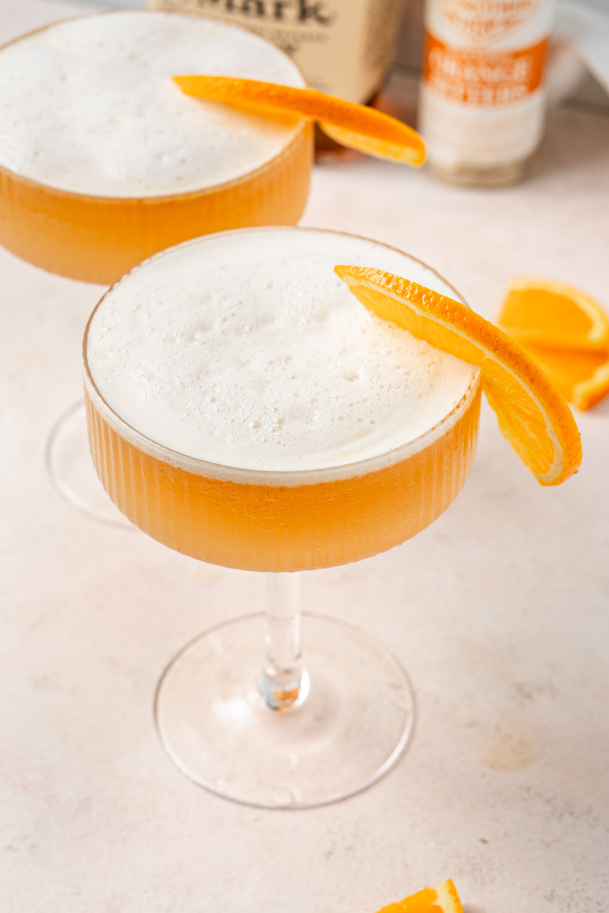 Gingerbread and orange whiskey sour in a coup glass with a frothy top.