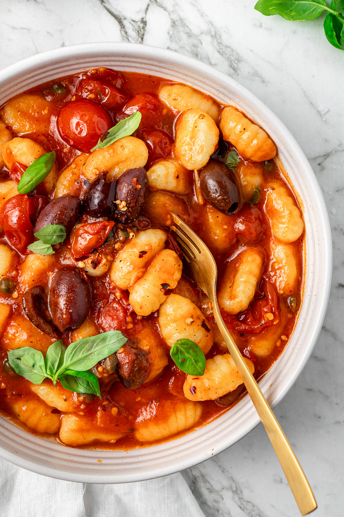 Close up of Vegan gnocchi puttanesca in a bowl with fresh basil and a fork.