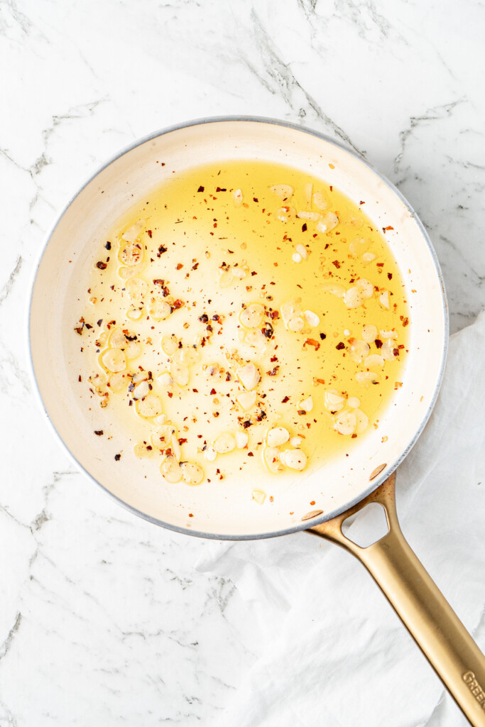 Heating the olive oil with garlic and chilli flakes in a frying pan.