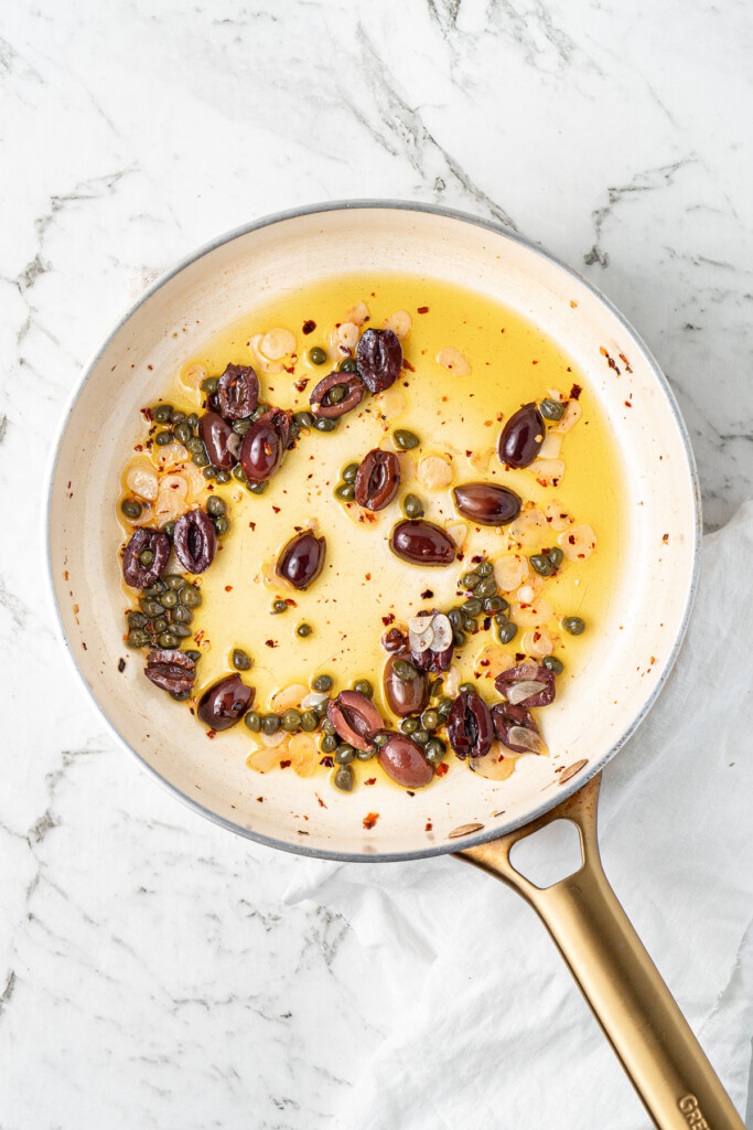 Adding the olives and capers to the frying pan.