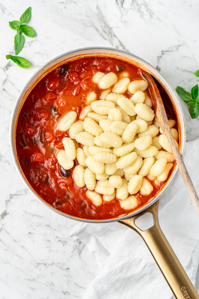 Adding the cooked gnocchi to the puttanesca sauce.