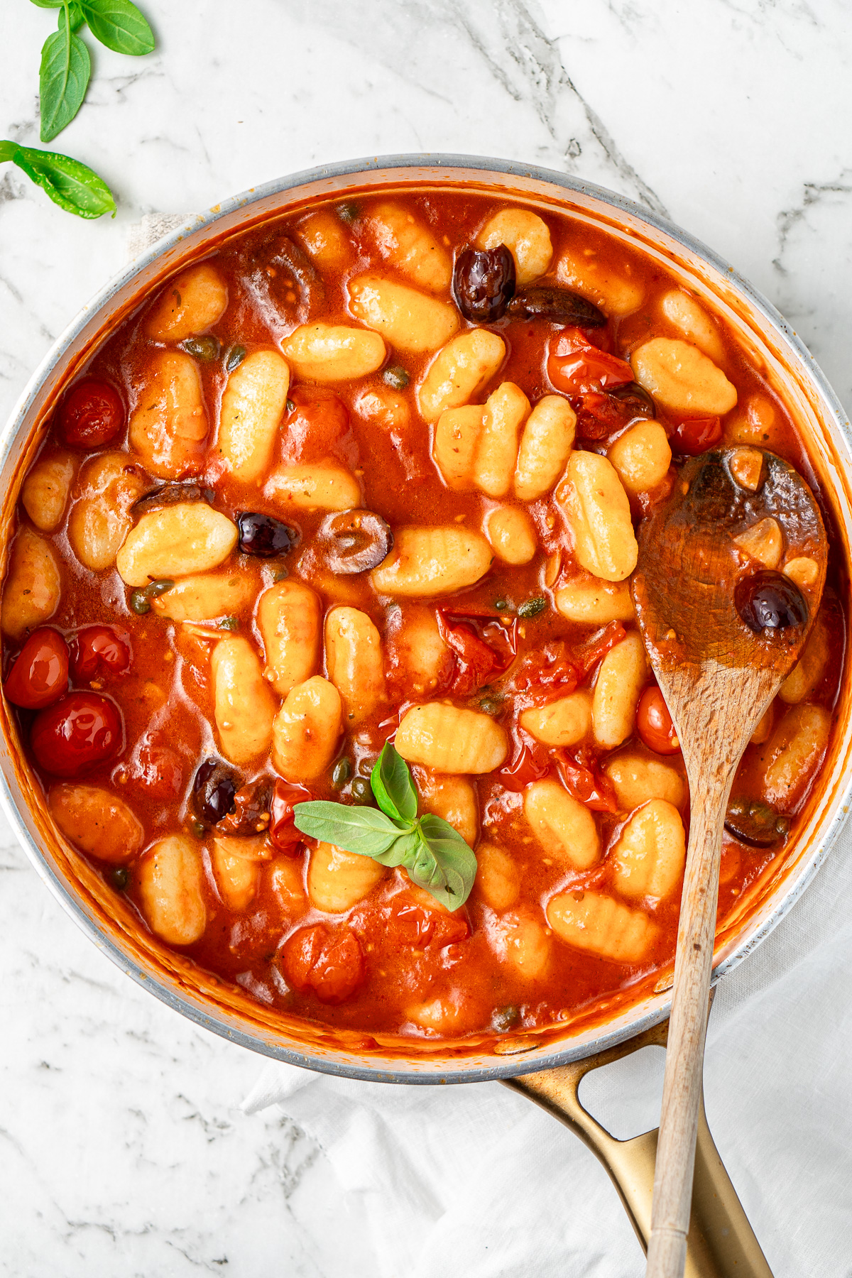 Close up of the gnocchi in the puttanesca sauce in a frying pan with a wooden spoon.