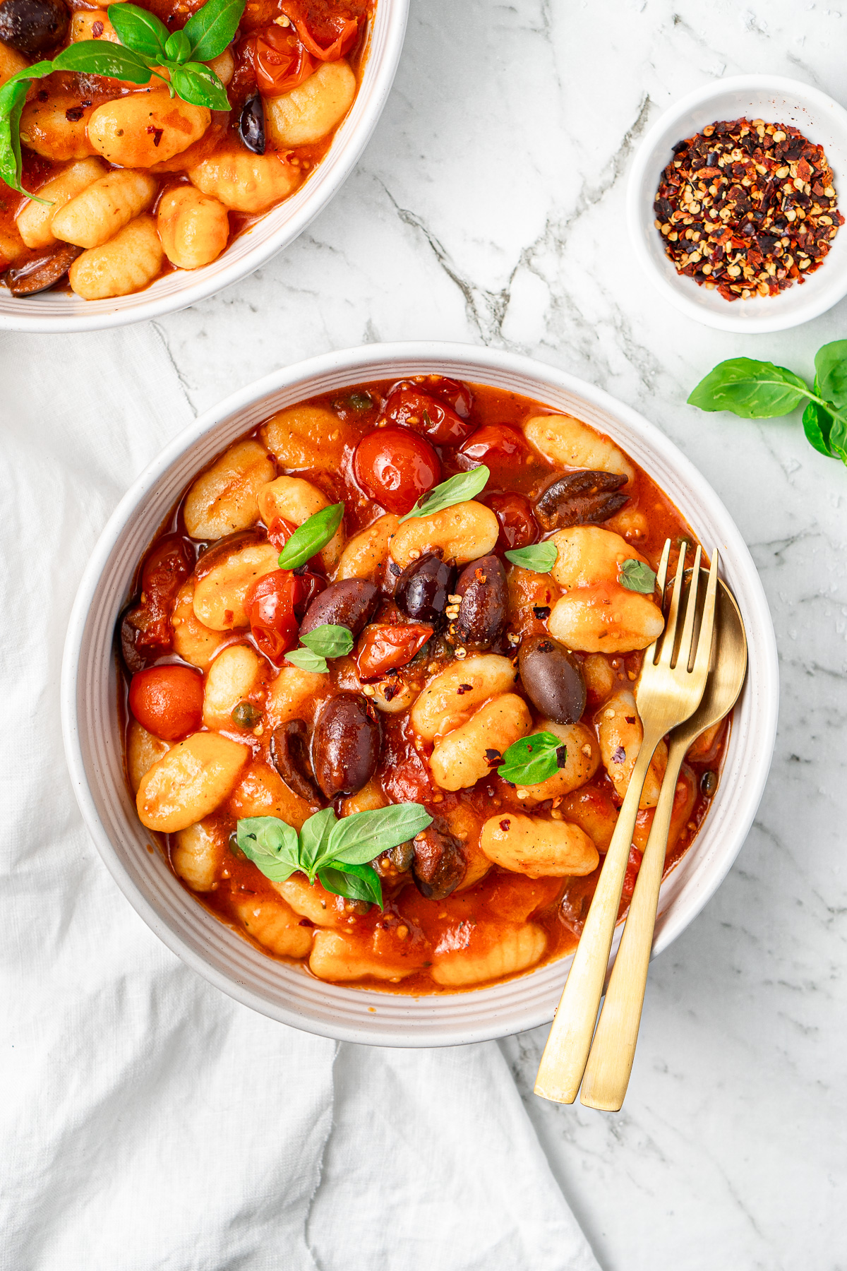 Vegan gnocchi puttanesca in a bowl with fresh basil.