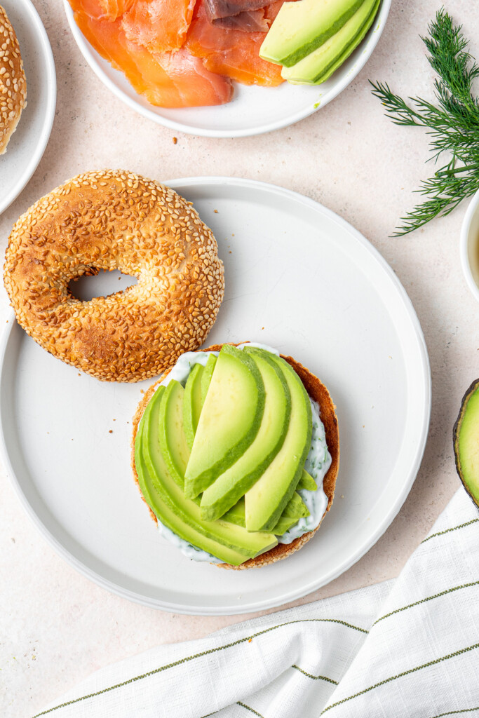 Adding sliced avocado to the bagel.