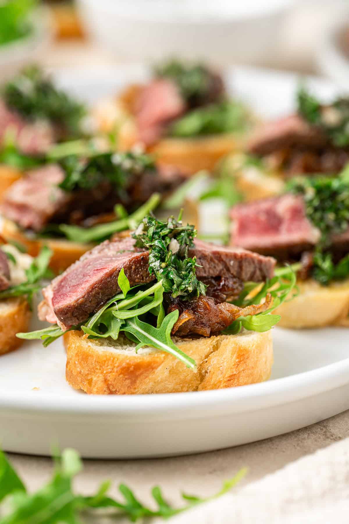 Close up of a steak crostini with rocket, caramelised onions and chimichurri. 