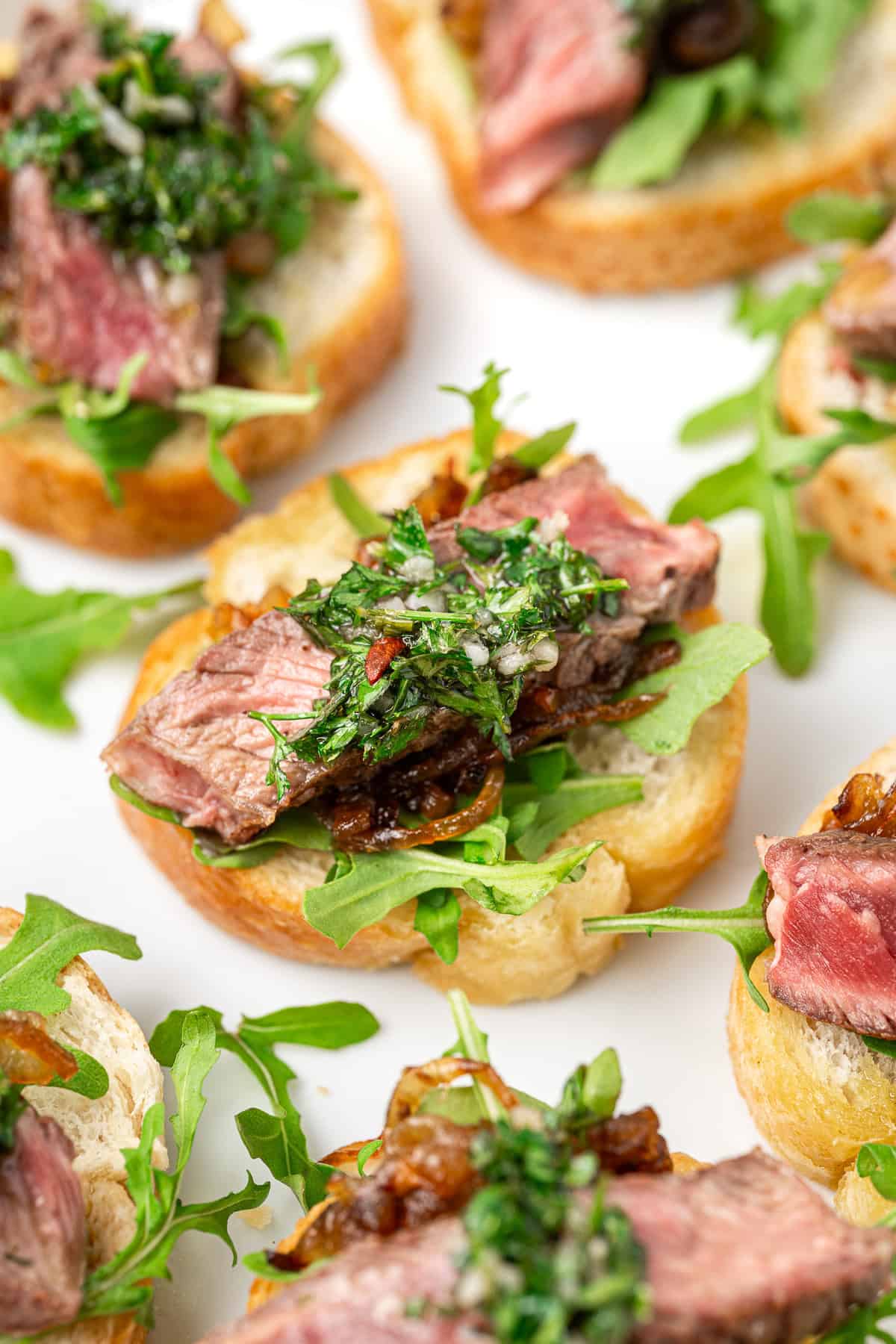 Close up of a steak crostini with chimichurri and caramelised onions. 