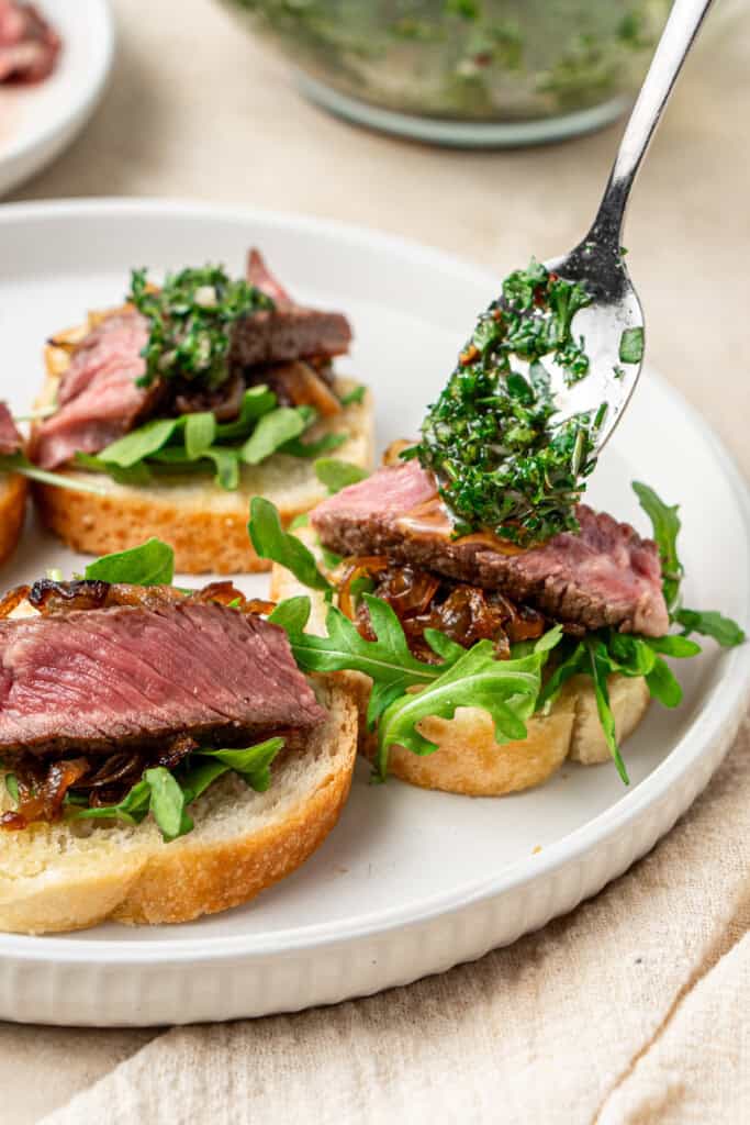 Spooning chimichurri over steak crostini. 