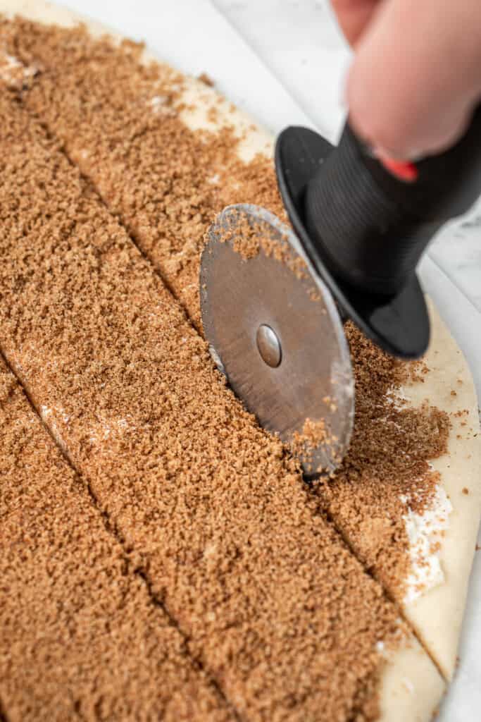 Using a pizza cutter to cut the dough into strips.