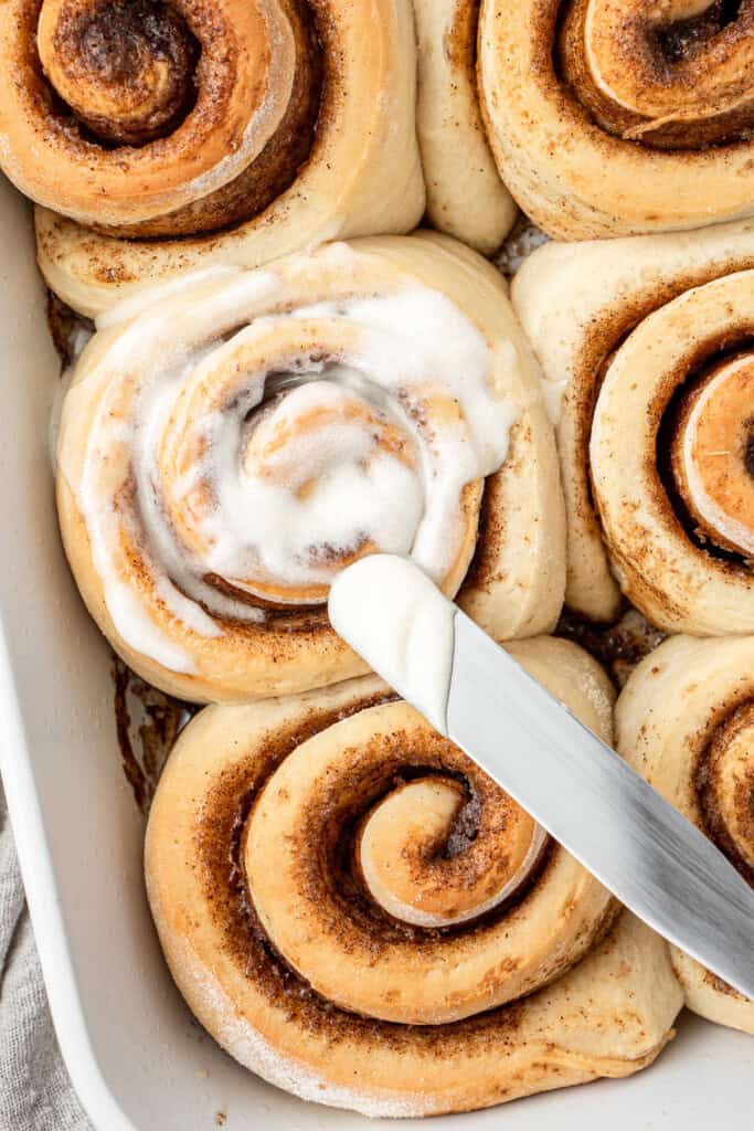 Spreading the icing over the cinnamon rolls.